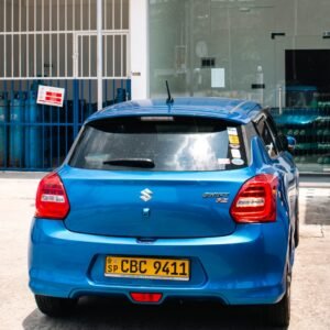 A blue suzuki swift parks in front of a building.